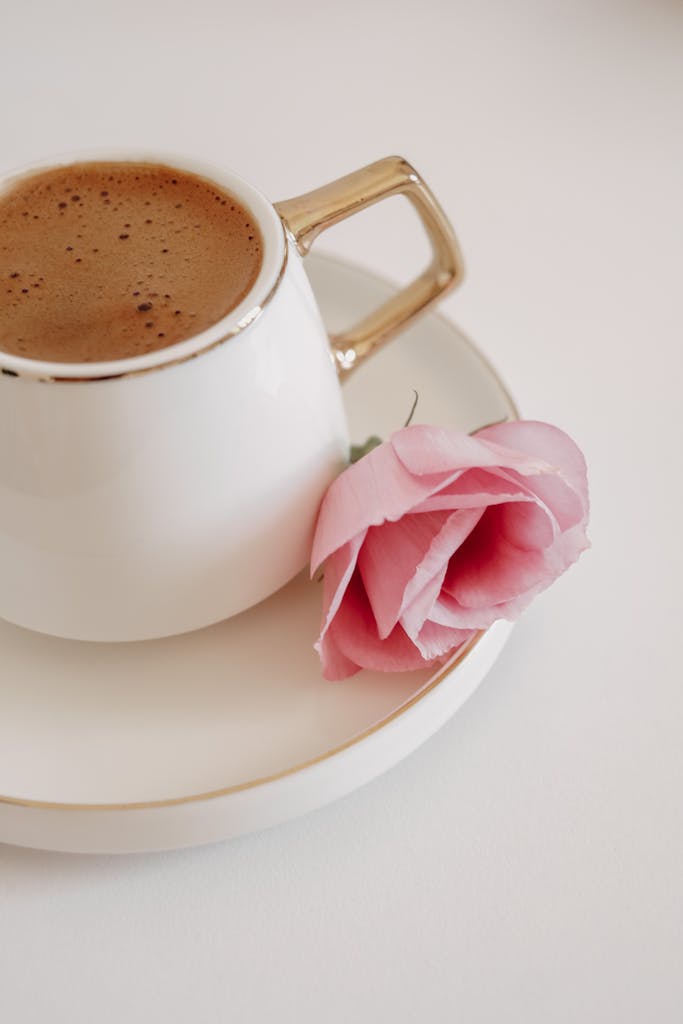 Close-up of a coffee cup on saucer with a pink rose, capturing elegance and simplicity.