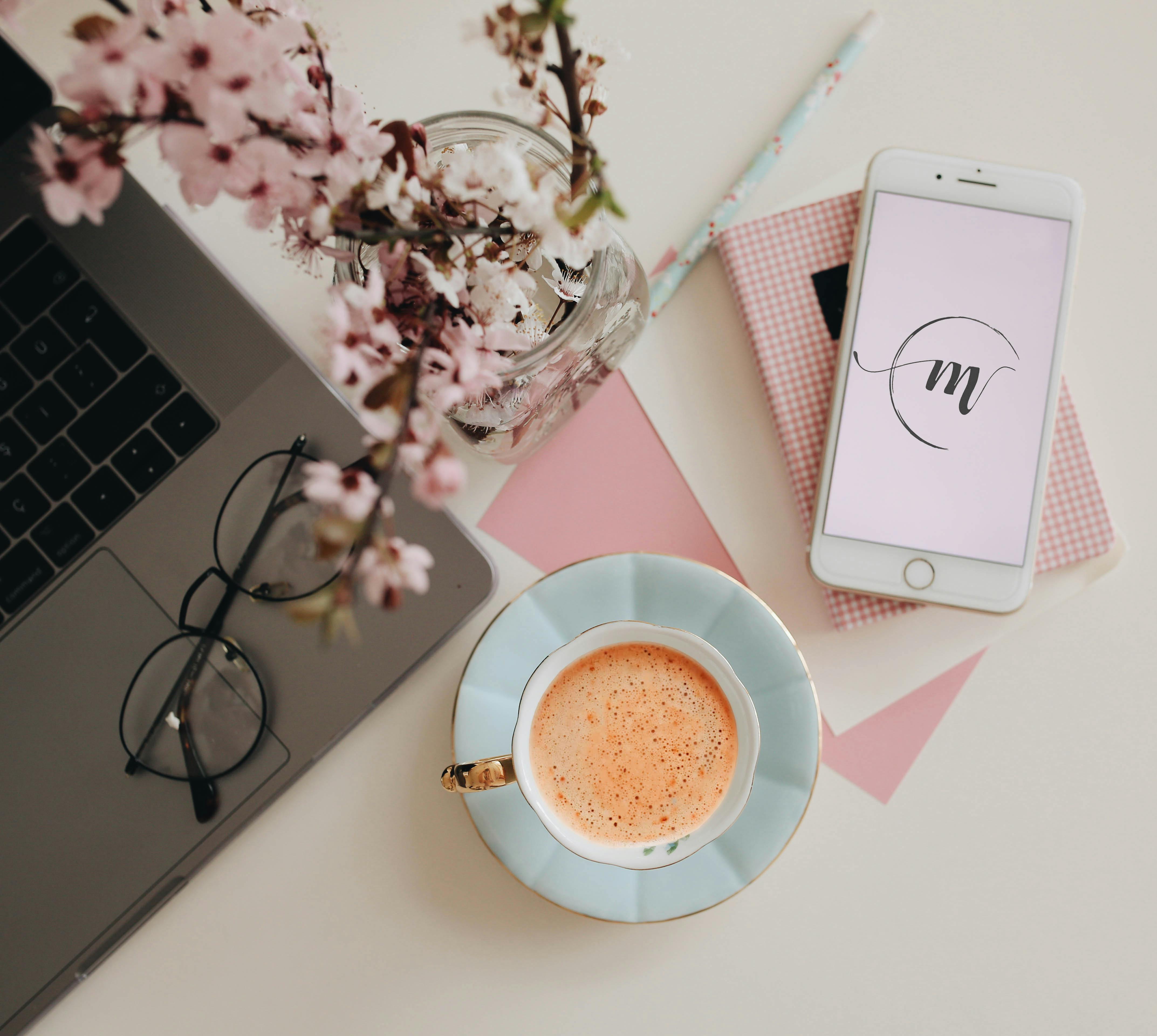 Chic workspace featuring a laptop, coffee, and cherry blossoms, perfect for creative inspiration.