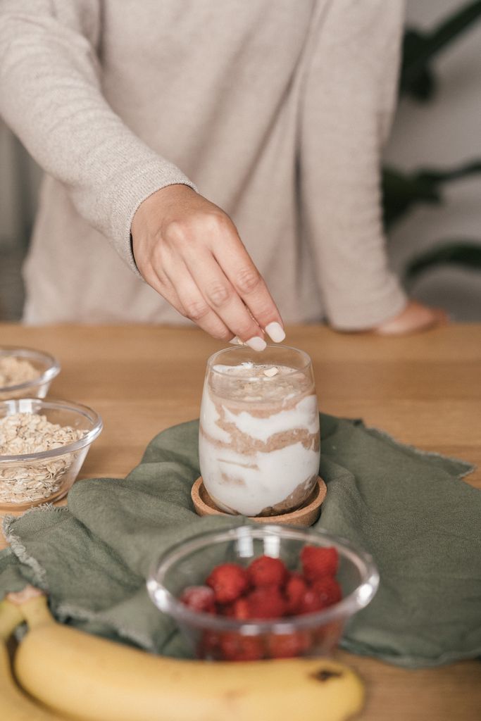 A hand garnishing yogurt and fruit parfait with healthy ingredients, captured in a cozy indoor setting.