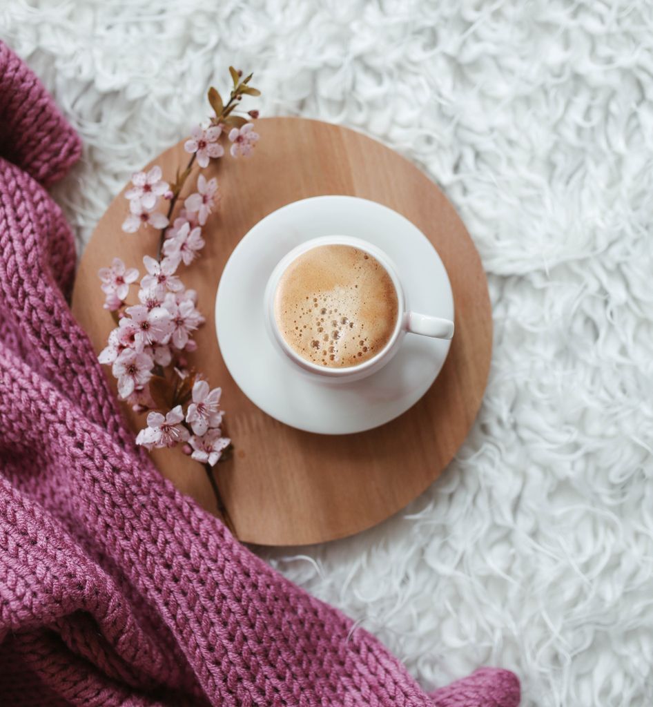 A warm cup of coffee with cherry blossoms on a wooden tray, perfect for a cozy setting.