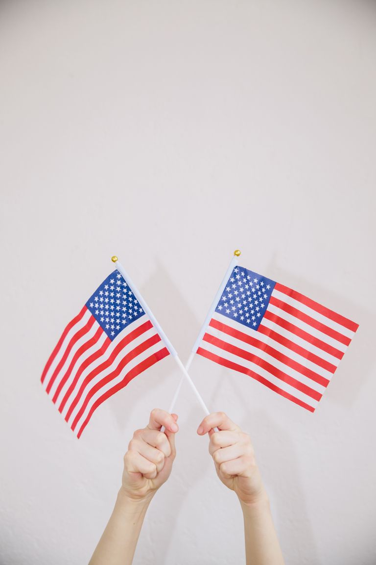 Two hands holding American flags symbolizing patriotism and celebration on a white background.