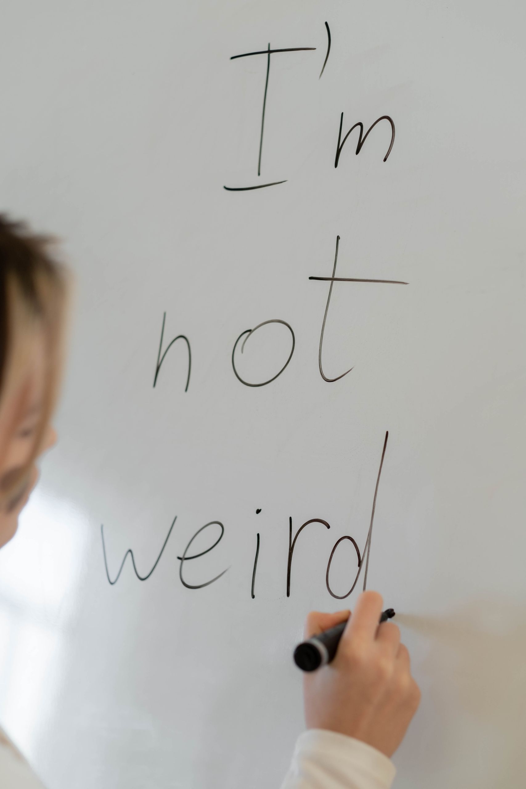 A child writes 'I'm not weird' on a whiteboard, promoting self-acceptance.