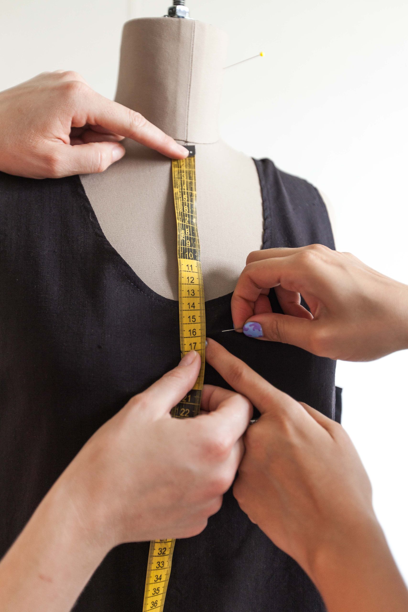 Close-up of hands using a tape measure on a mannequin wearing a black dress. Fashion concept.
