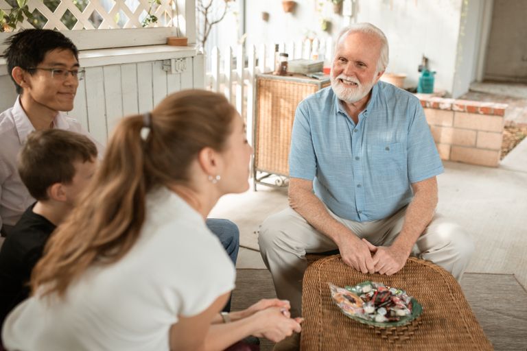 Elderly man enjoying a pleasant family gathering outdoors with diverse group sitting together.