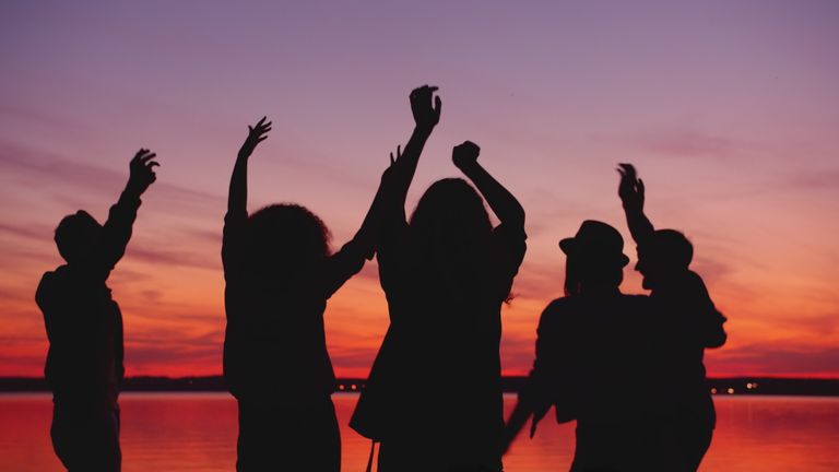 Silhouettes of people raising hands in celebration against a colorful sunset.